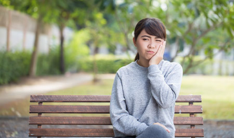 woman on a park bench in pain holding her jaw