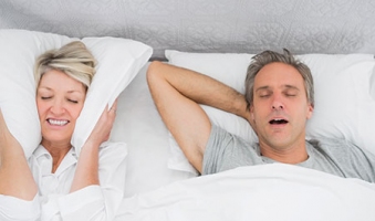 woman covering her ears with pillow while her partner is asleep snoring