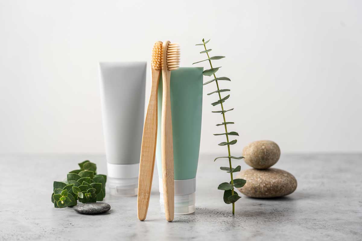 Bamboo toothbrushes and tubes of toothpaste on white background. Eucalyptus branches. Natural dental care concept. Side, close up view