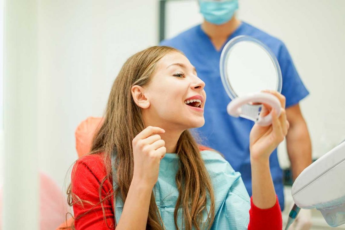 Young woman checking their teeth at mirror after dental treatment